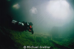 A diver in side-mount gear returns to the warm sunlit ent... by Michael Grebler 